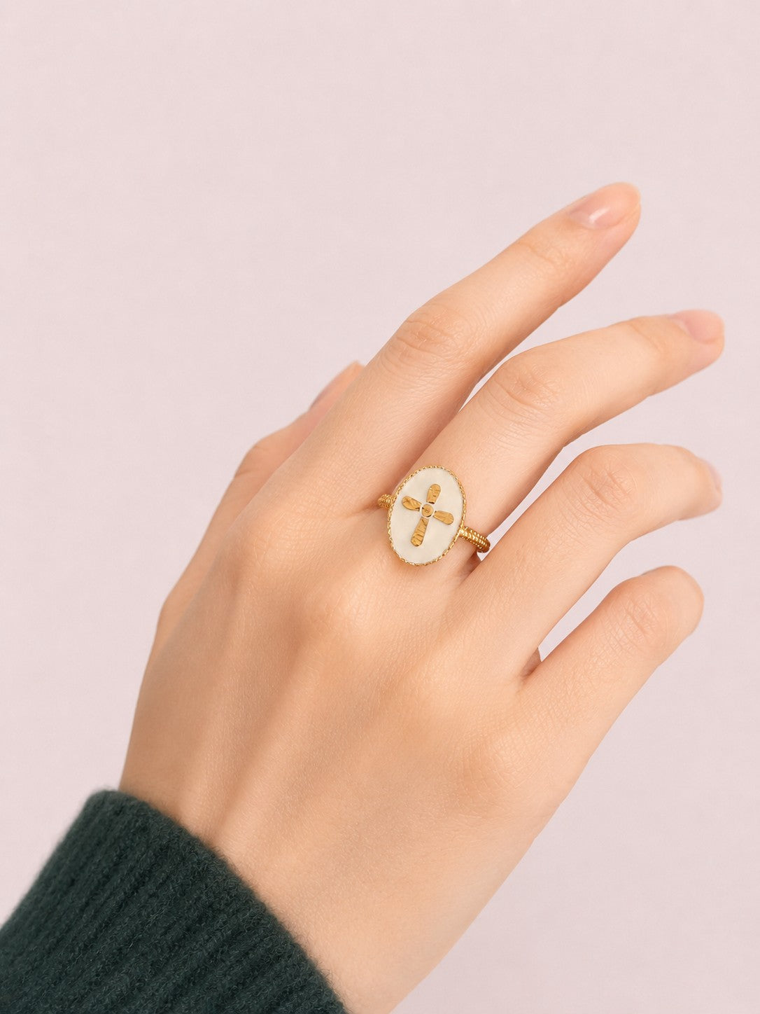 Bague Croix Nacrée portée sur la main avec finition dorée et fond minimaliste