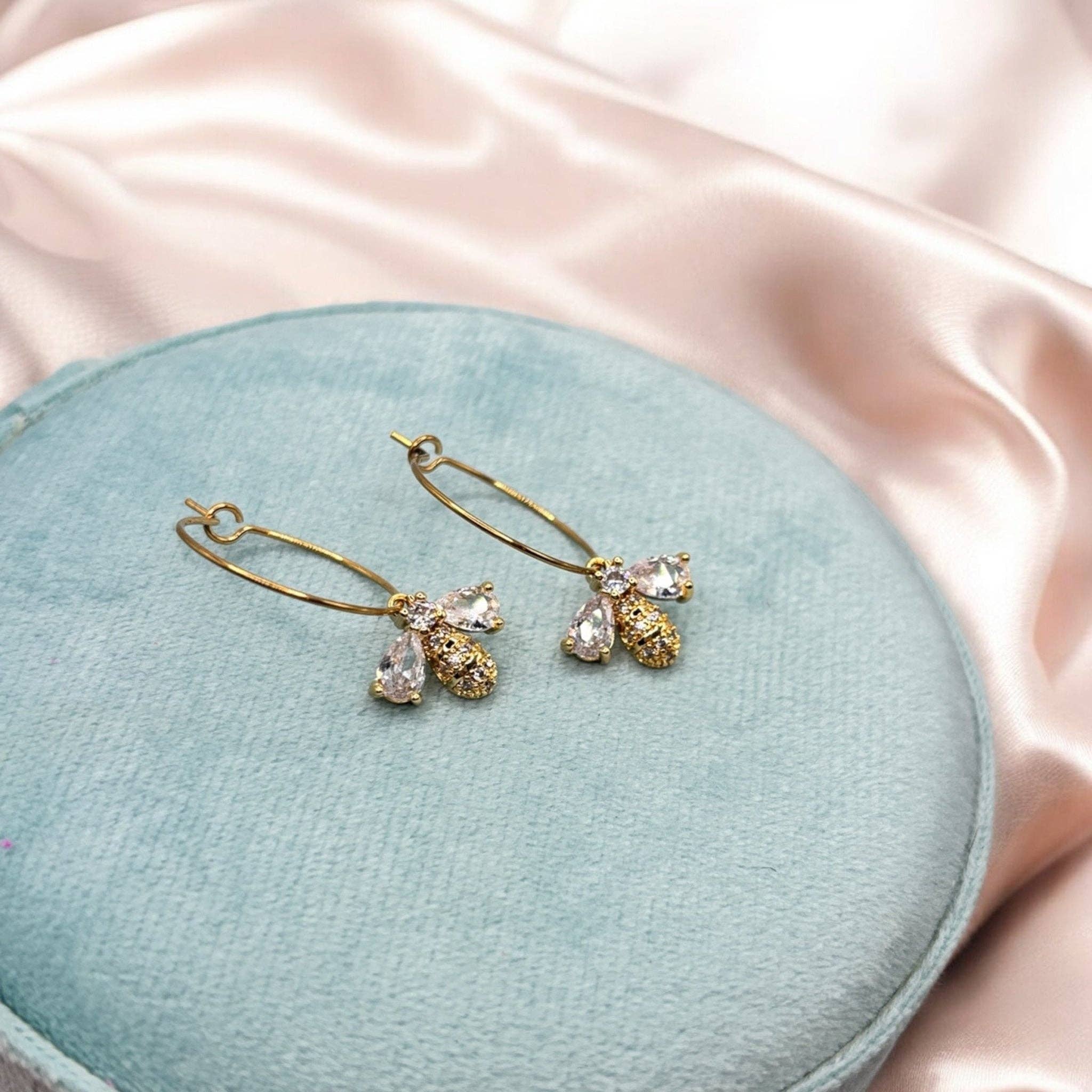Boucles d’oreilles Abeille Divine dorées en laiton plaqué or décorées de zircons sur fond rose et bleu