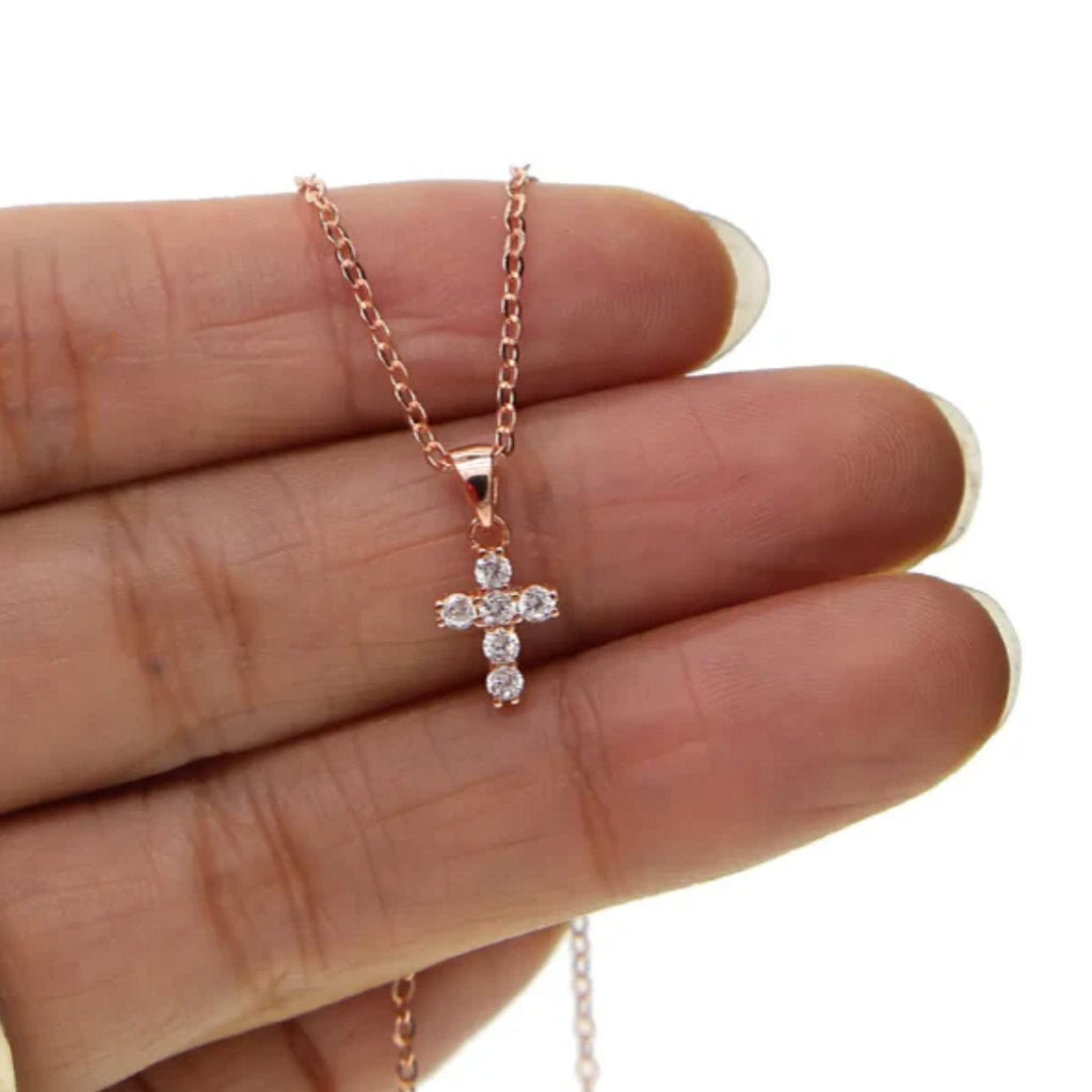 Collier croix Ève en or rose présenté dans la main